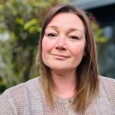 Sarah Brownlie, Director of Development at KWT, smiling in front of a green backdrop.